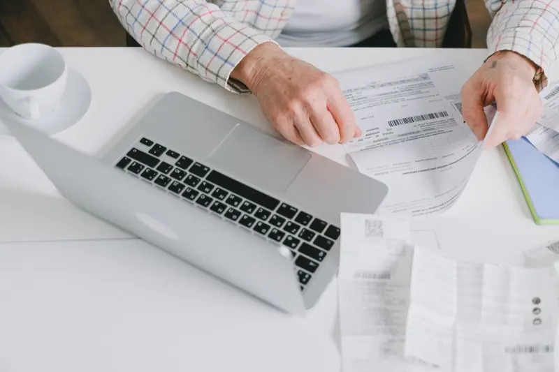 Mains classant des documents et justificatifs de frais professionnels sur un bureau à côté d'un ordinateur portable