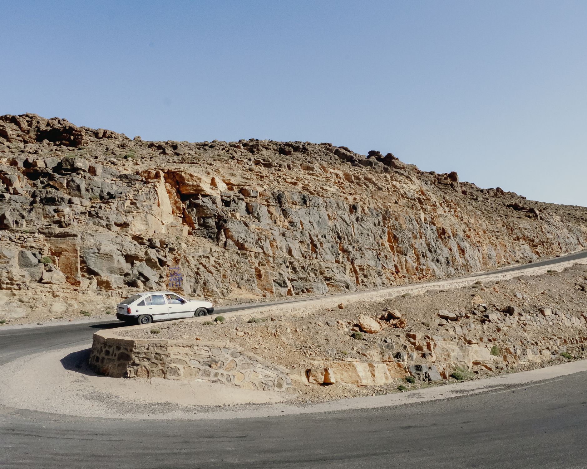 voiture blanche dans un virage en épingle d'une route de montagne rocailleuse de l'Atlas marocain