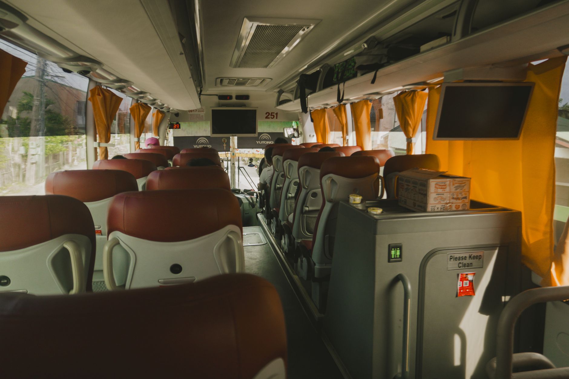 intérieur d'un autocar de tourisme avec rangées de sièges en cuir, écrans au plafond et pictogramme des toilettes à bord