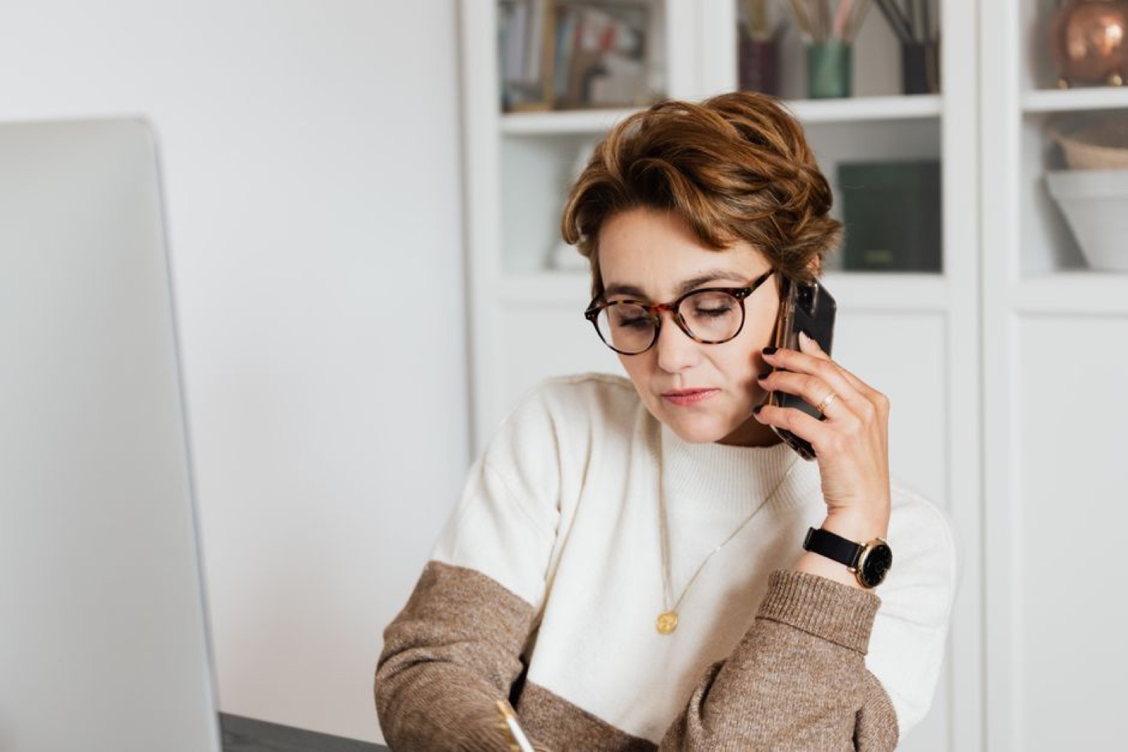 Femme avec des lunettes au téléphone devant un ordinateur portable, à son bureau